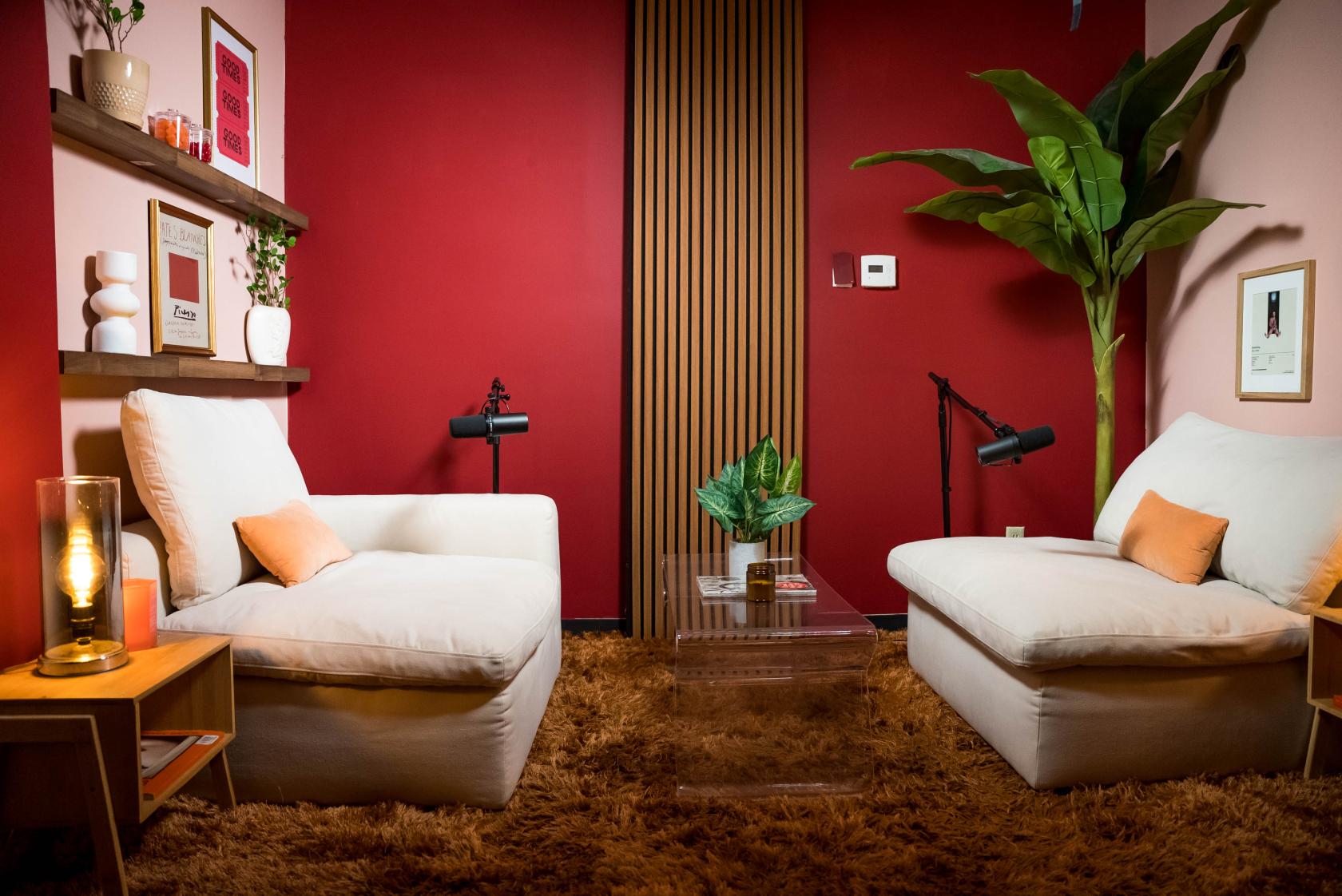 A podcast studio with plush chairs, table microphones, shaggy carpet, and red accent walls at Lazy Pickle Studios - BURBANK.