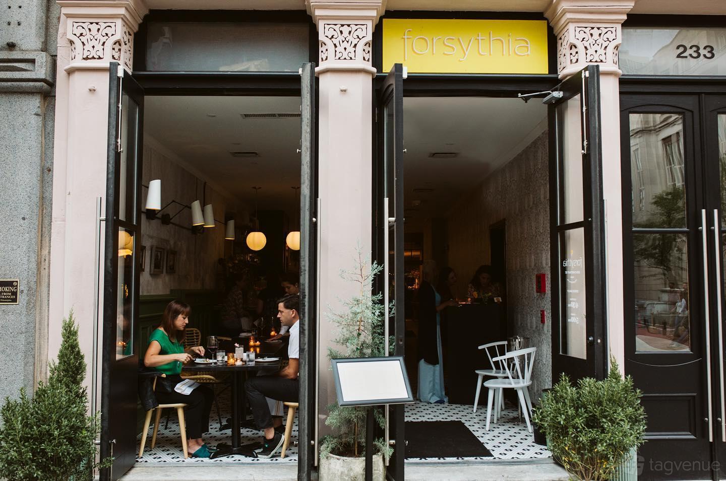 A restaurant with an open entrance, small tables, and black-and-white tile flooring at Forsythia.