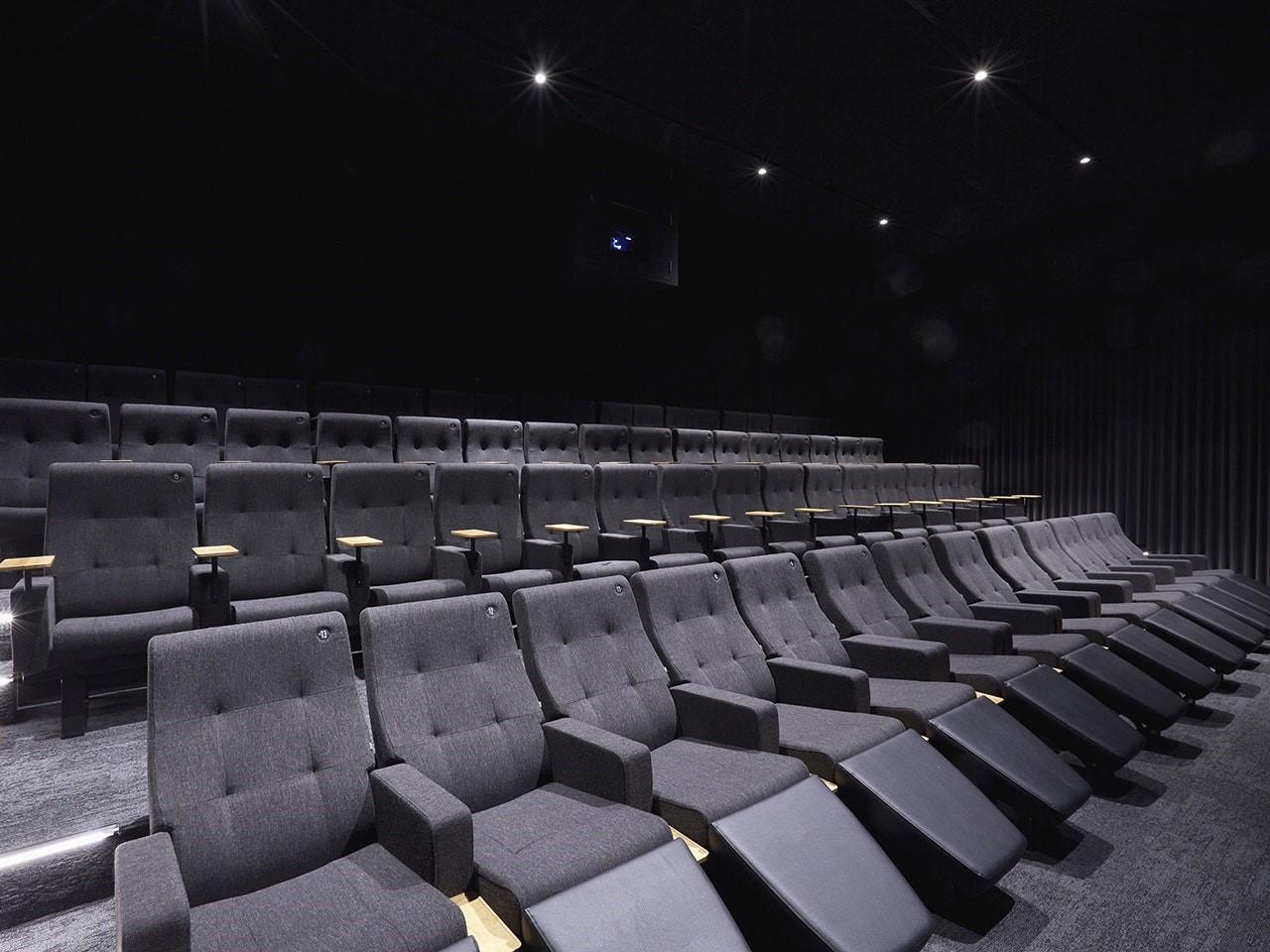 A cinema with tiered rows of plush gray seats and small wooden arm tables at Curzon Hoxton.