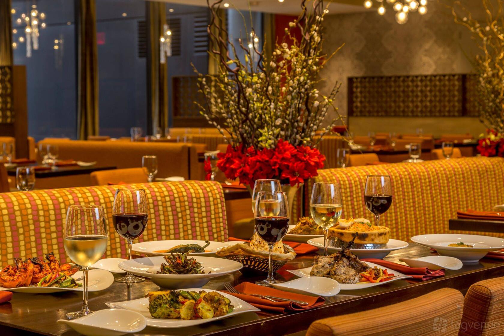 A restaurant dining area with upholstered seating, floral centerpieces, and tables set with wine glasses and Indian dishes at Utsav.
