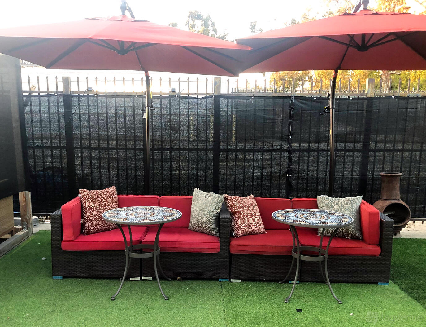 An outdoor lounge with red cushioned sofas, patterned pillows, two mosaic tables, and large umbrellas at The Creative House.