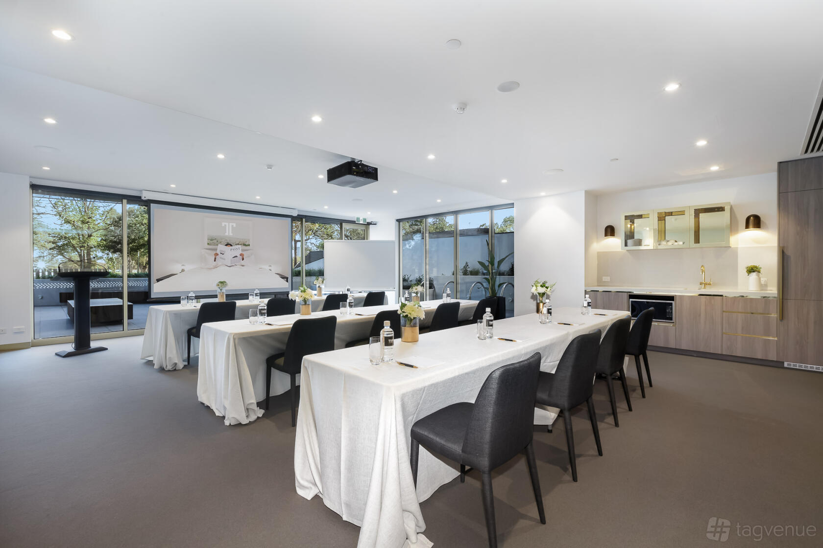 A conference centre with floor-to-ceiling windows, projector, and tables with white linens at Tyrian.