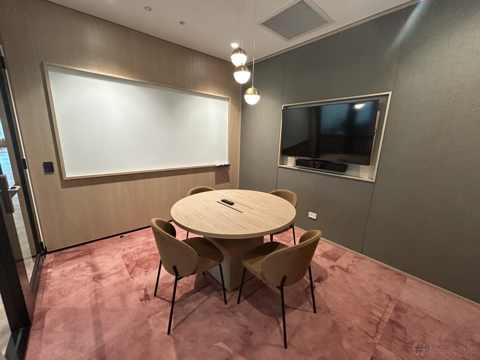 A meeting centre with a round table, four chairs, wall-mounted screen, and large whiteboard at JustCo at King Street.