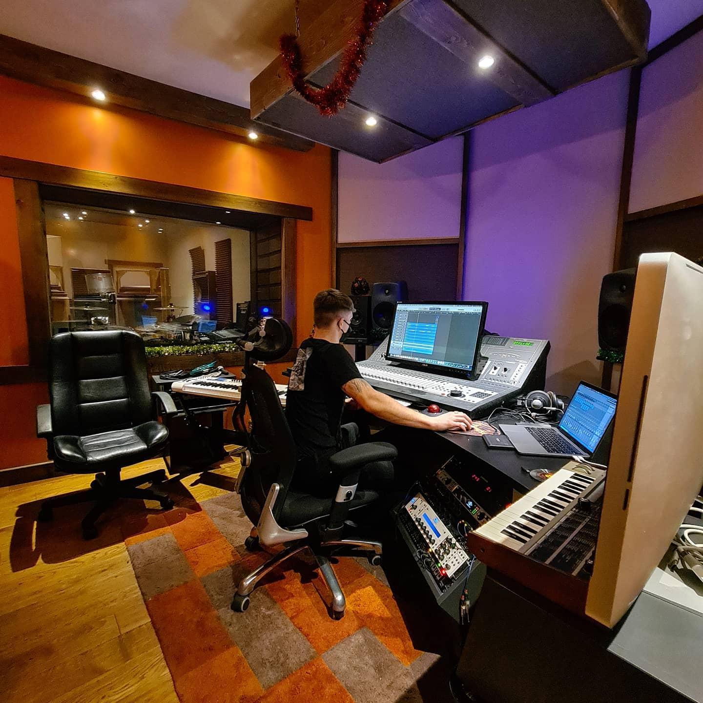 A recording studio with a large mixing console, computer monitors, keyboards, and acoustic panels at Vibratone Sound Studio.
