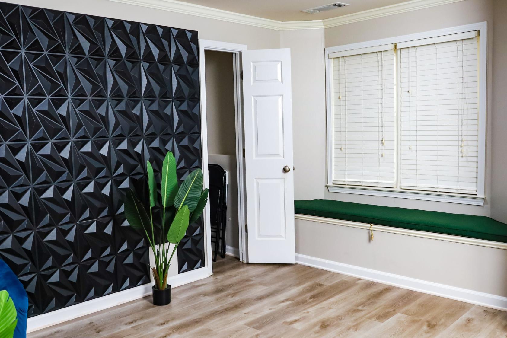 A photo studio with a geometric black accent wall, wood floors, a green bench, and a large potted plant at High Arc Studio.