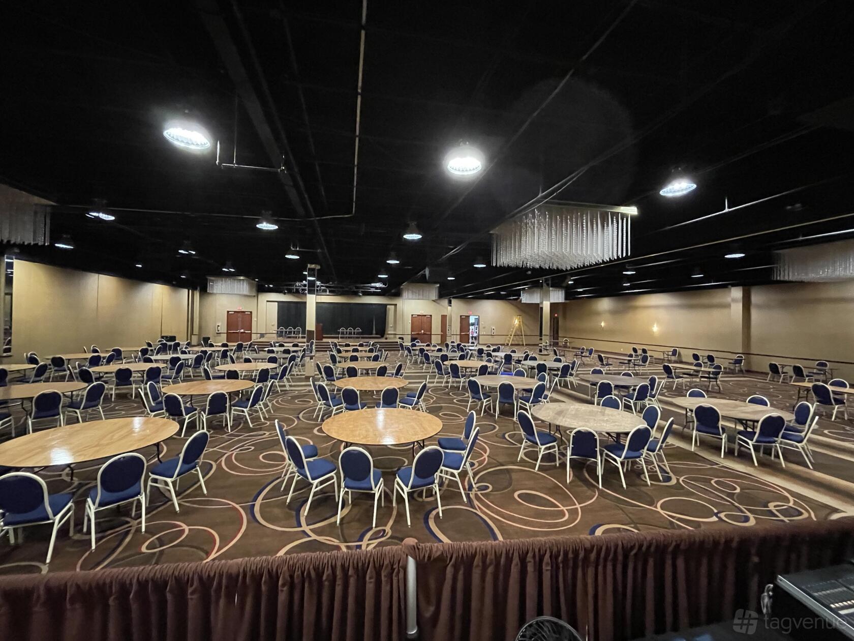 A spacious ballroom with round tables, blue cushioned chairs, patterned carpet, and ceiling chandeliers at The Community Collective for Houston.