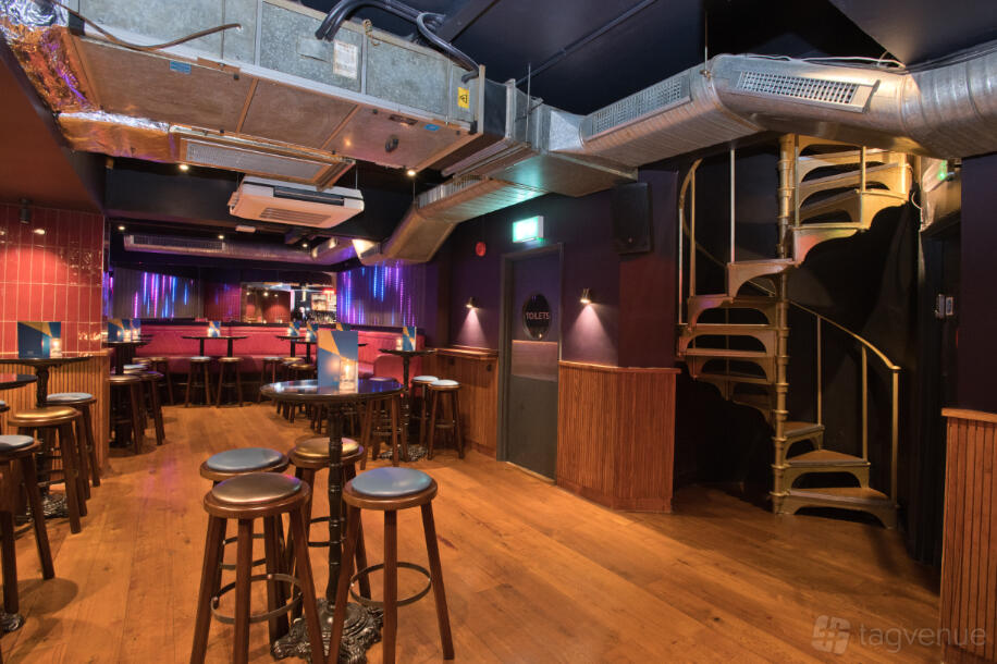 An event space in a cocktail bar with wooden floors, high stools, and a spiral staircase at Be At One Farringdon.