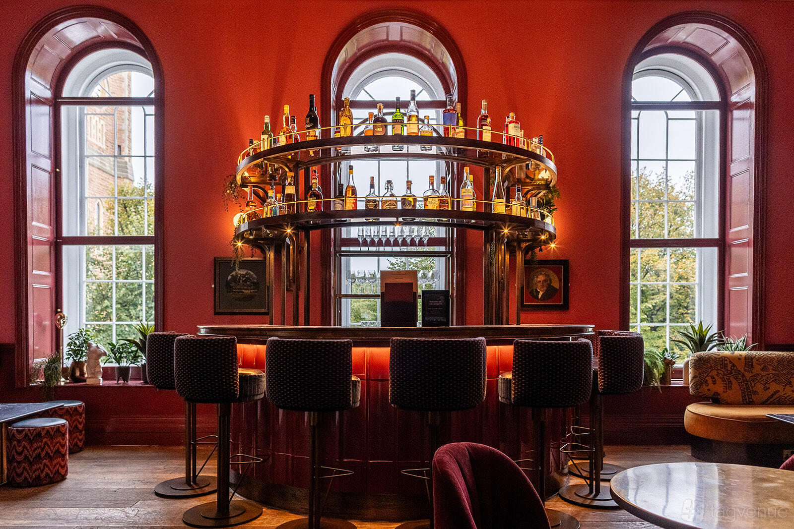 An event venue with an ornate circular bar, high-backed stools, arched windows, and red walls at Kindred.