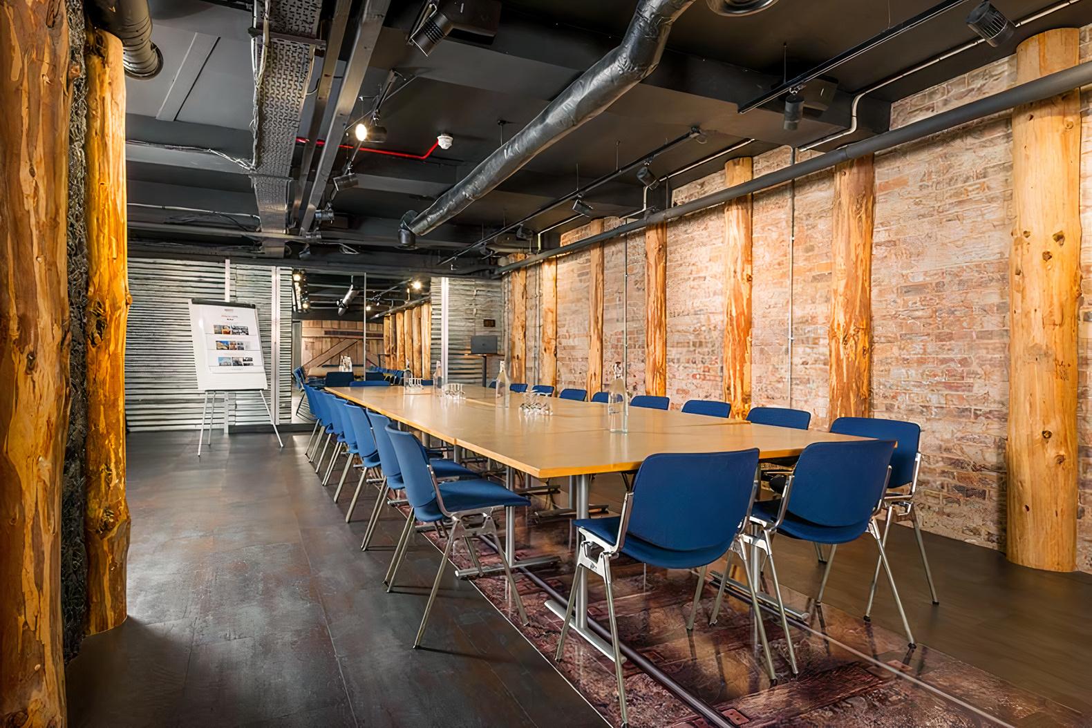 A meeting room with exposed brick walls, wooden columns, and blue chairs around a central table at 297 Euston Road.
