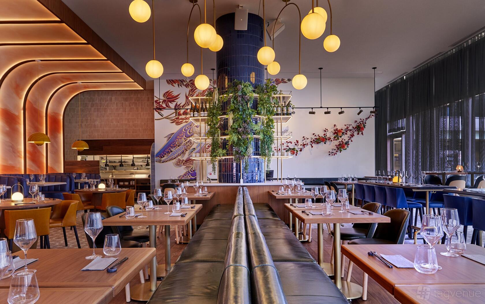 A dining room with glass-topped tables, leather banquettes, globe pendant lighting, and a plant-covered pillar at Minami Toronto.