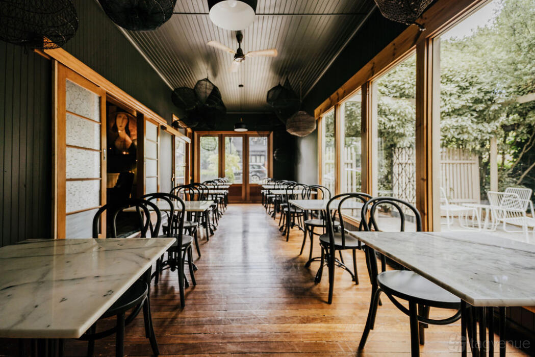 A hotel event room with marble-topped tables, bentwood chairs, wood floors, and floor-to-ceiling windows at The Amalfi.