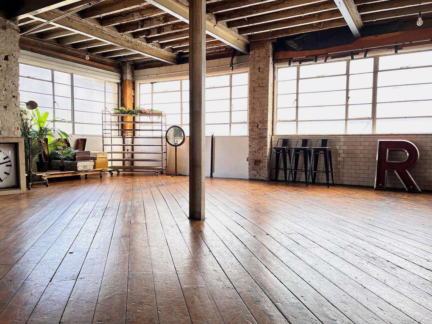 A photo studio with large factory windows, exposed beams, wood floors, and vintage decor at Belt Craft Studios.