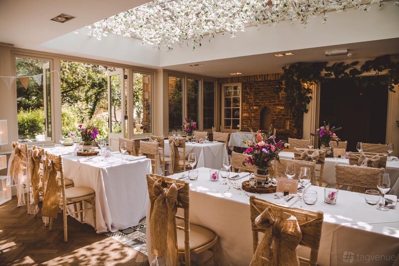 A conservatory with long banquet tables draped in white linens, floral centerpieces, and a glass ceiling at Old Rectory House.