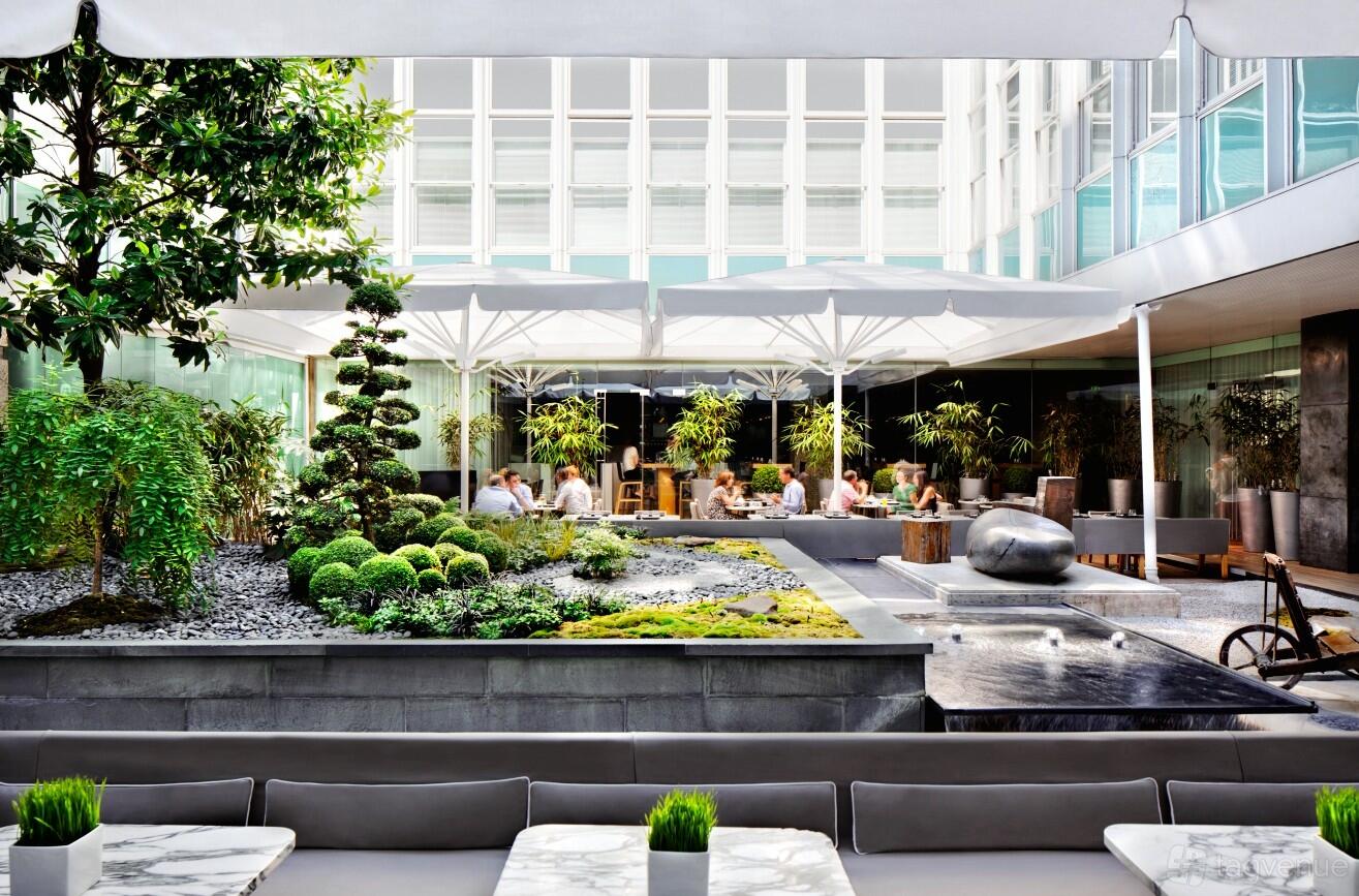 An outdoor hotel courtyard with manicured greenery, water features, and large white umbrellas at Sanderson London.