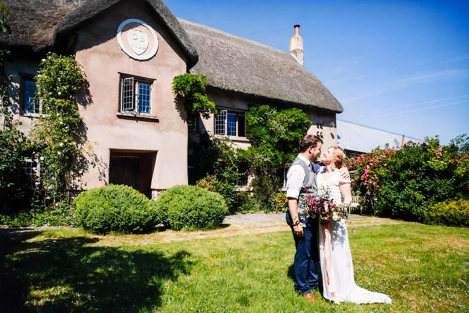 A barn venue with a thatched roof cottage, climbing ivy, and landscaped gardens at Hayne Devon.