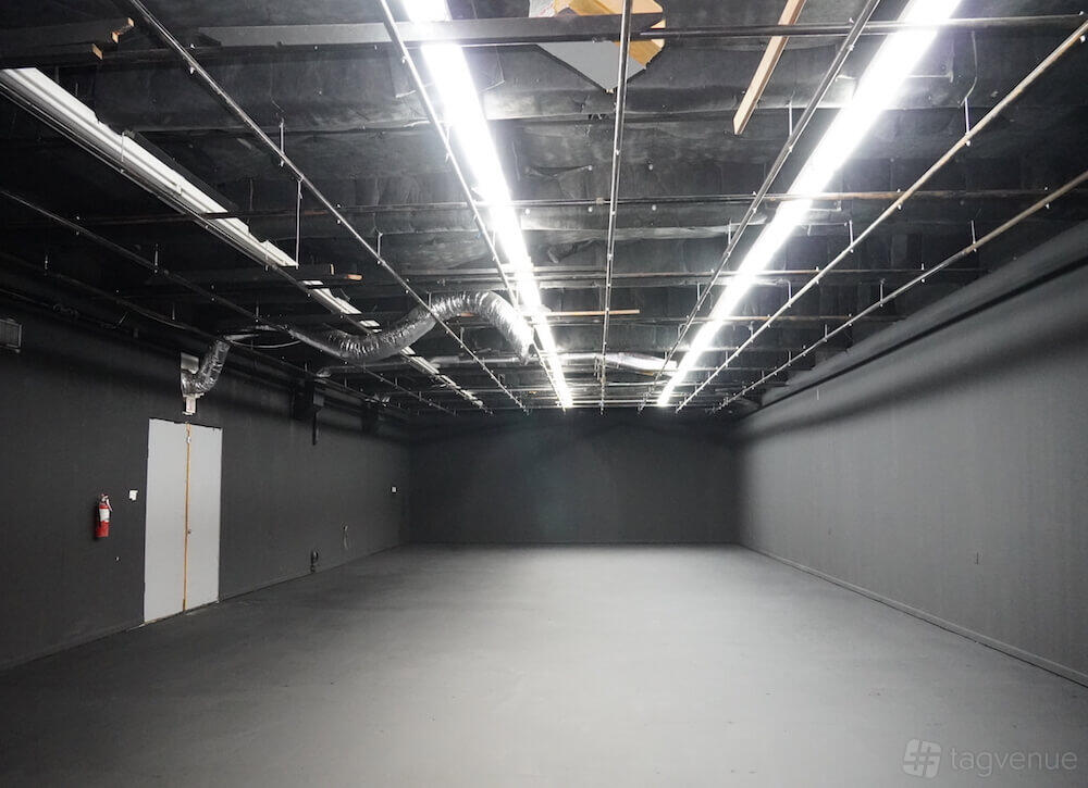 A photo studio with black walls, exposed ceiling fixtures, and fluorescent strip lighting at M3 Studios.