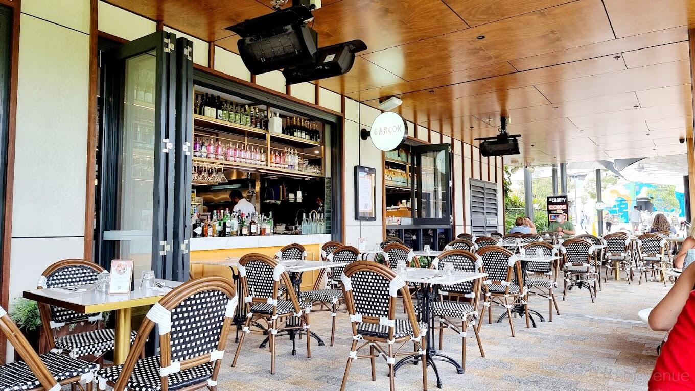 A restaurant terrace with woven bistro chairs, round tables, and an open bar area at Garçon Lane Cove.