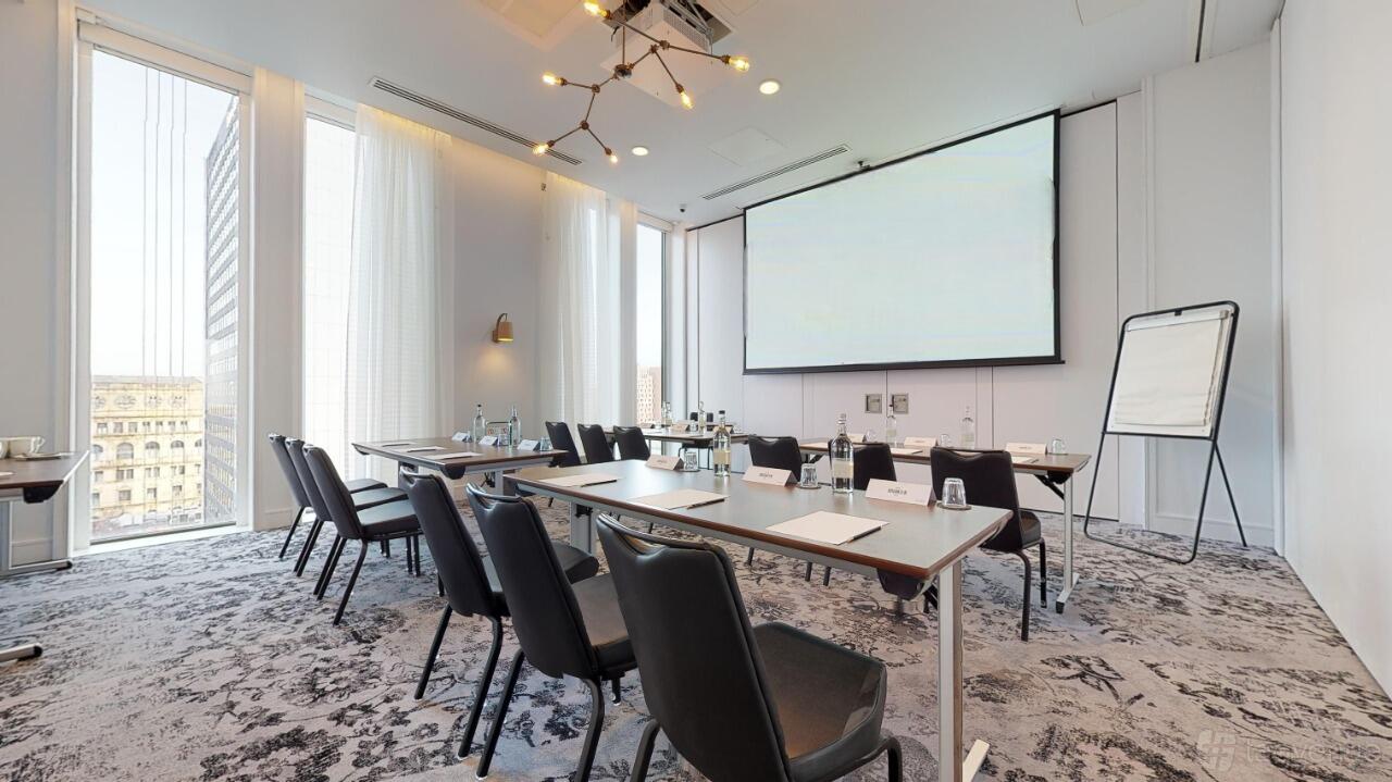 A meeting room with floor-to-ceiling windows, modern lighting, and a large projector screen at voco Manchester