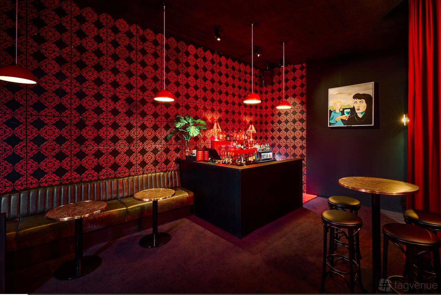 A nightclub bar with patterned red wallpaper, red pendant lighting, and velvet booth seating at Carousel Bar & Ballroom.