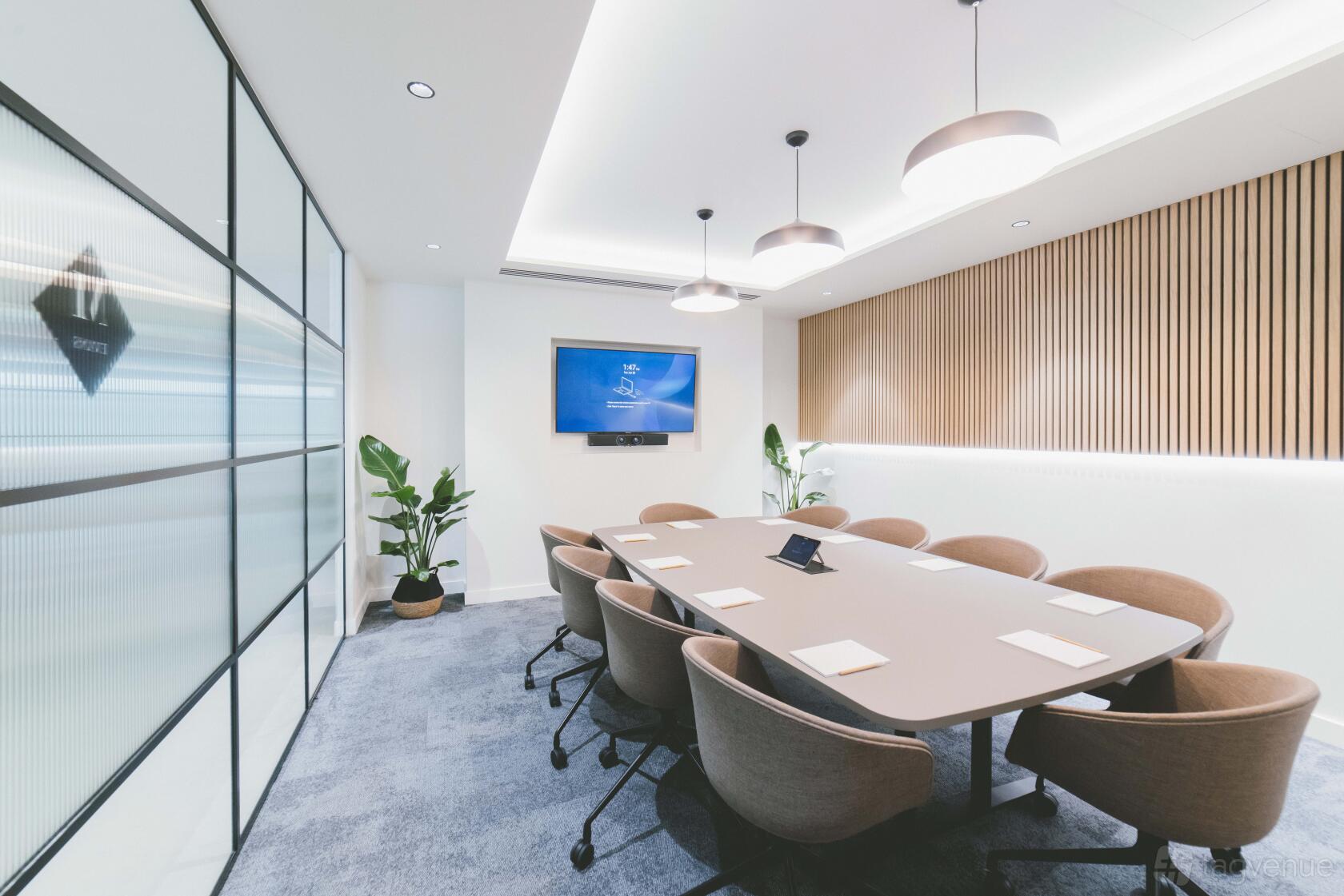 A boardroom with a large conference table, modern chairs, wall-mounted screen, and plants at Orega Marlow.