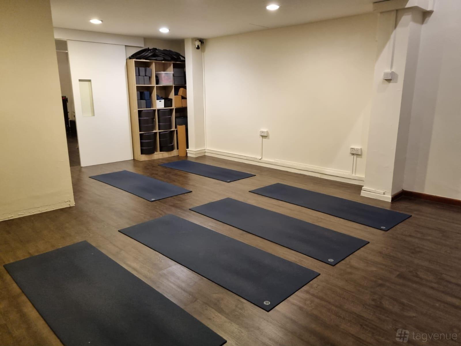 A dance studio with yoga mats on wood floors and storage shelves at Shiva Yoga Studio.