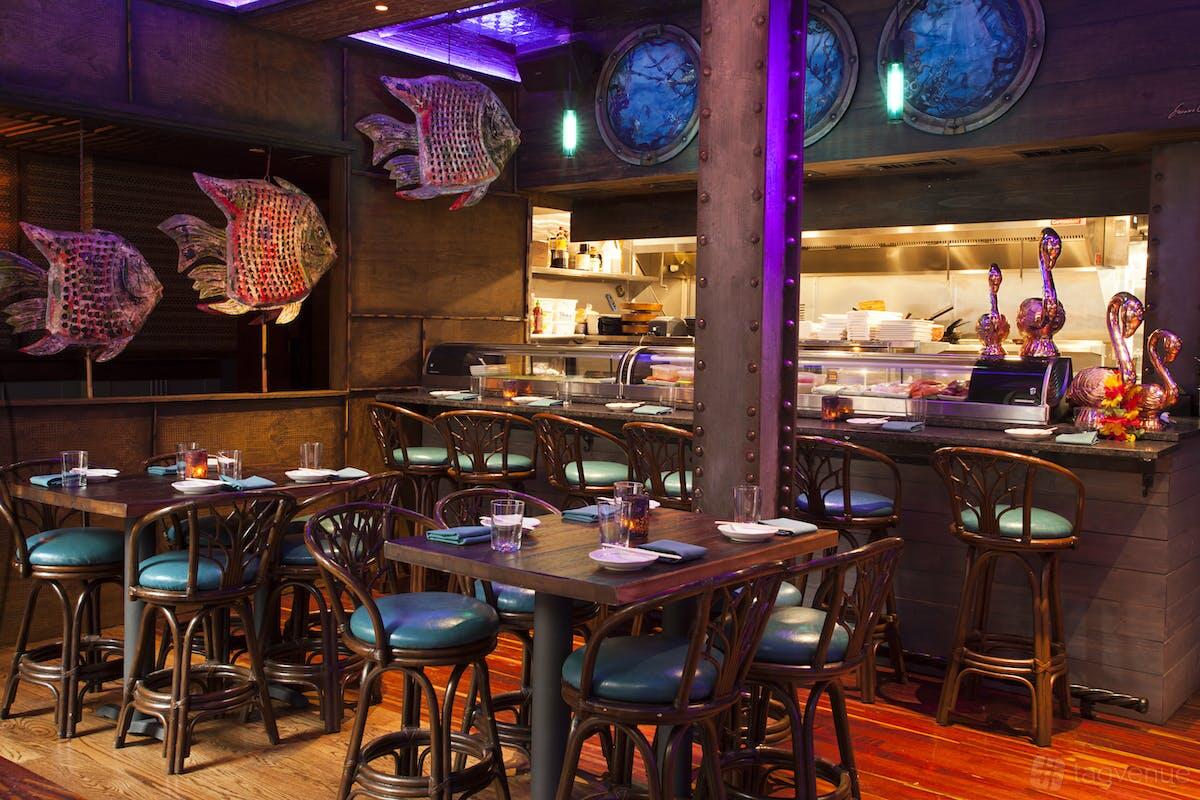 A restaurant with tropical decor, colorful fish sculptures, and open kitchen seating at Tiki Rock.