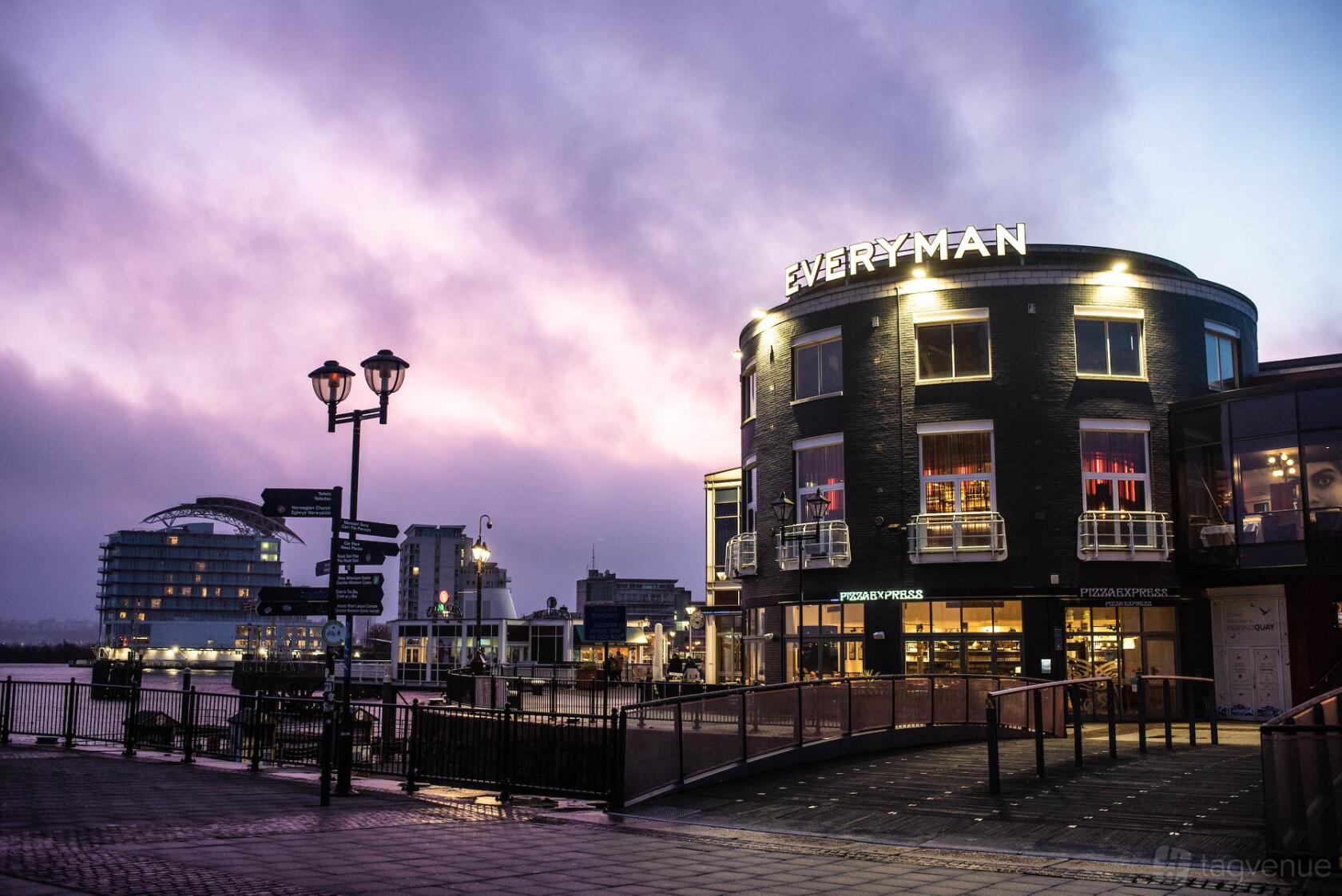 A cinema with curved black brick exterior, large windows, and illuminated signage at Everyman Cardiff.