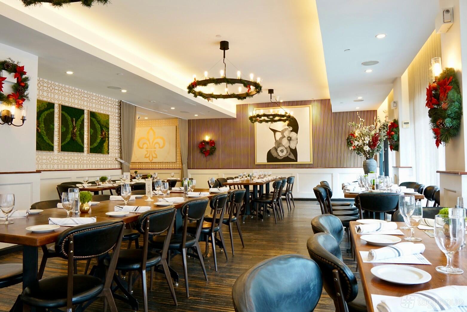 A dining room with long wooden tables, black leather chairs, large floral arrangements, and festive wreaths at Copinette.