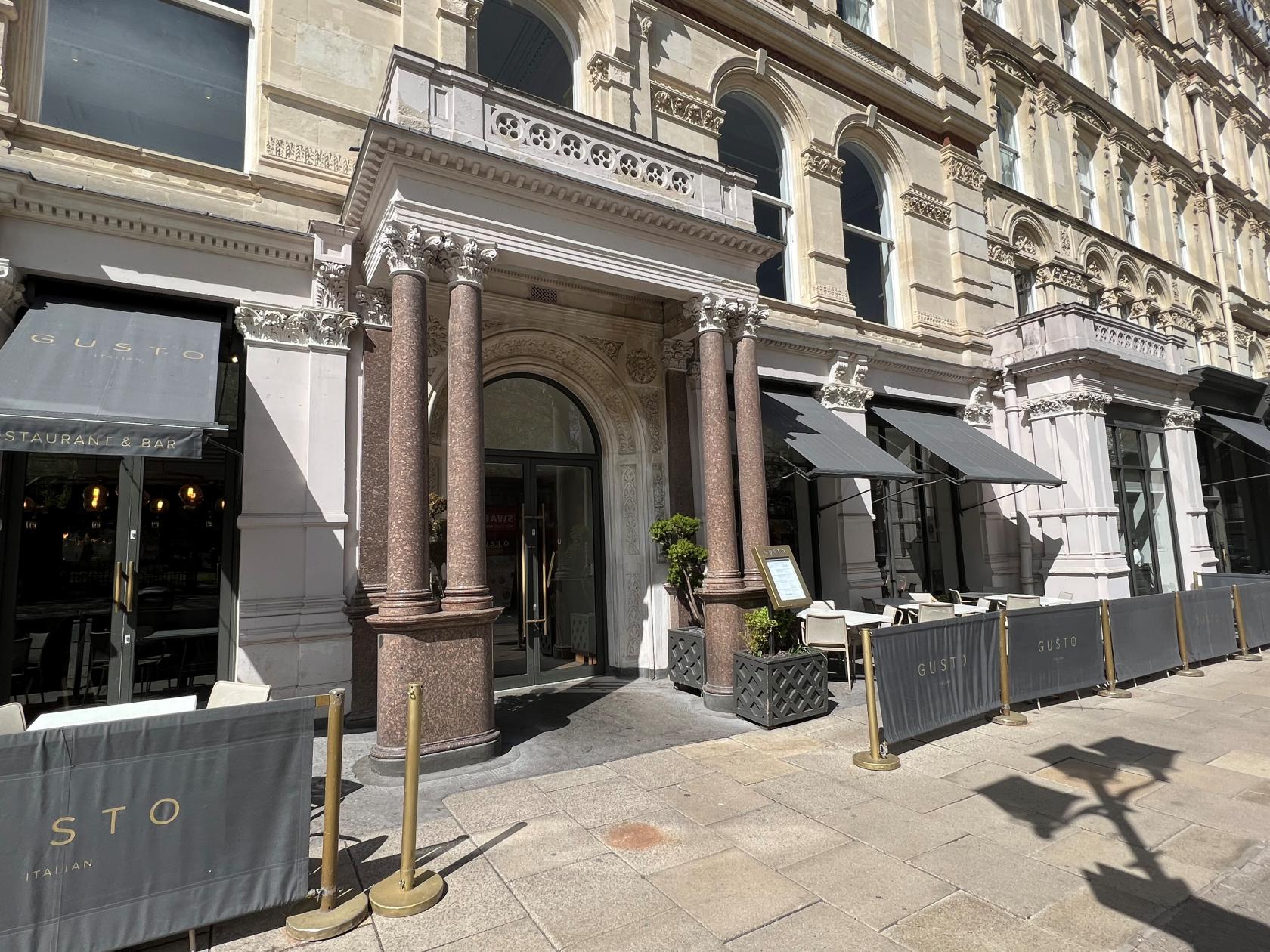 A restaurant with a stone façade, tall columns, and outdoor seating along the sidewalk at Gusto Italian, Birmingham.