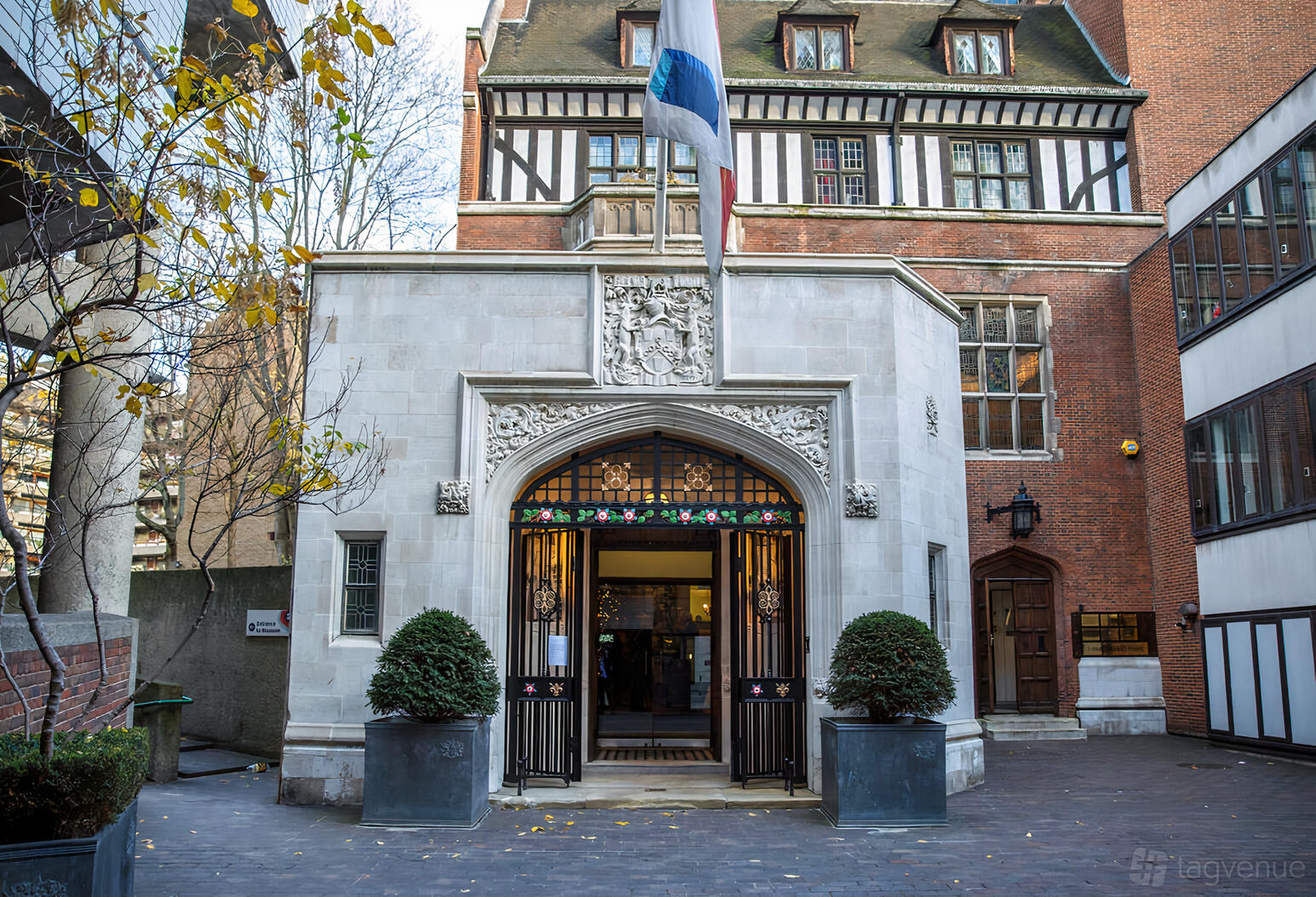 A historic hall with a stone entrance, arched doorway, decorative iron gate, and flag at Ironmongers' Hall.