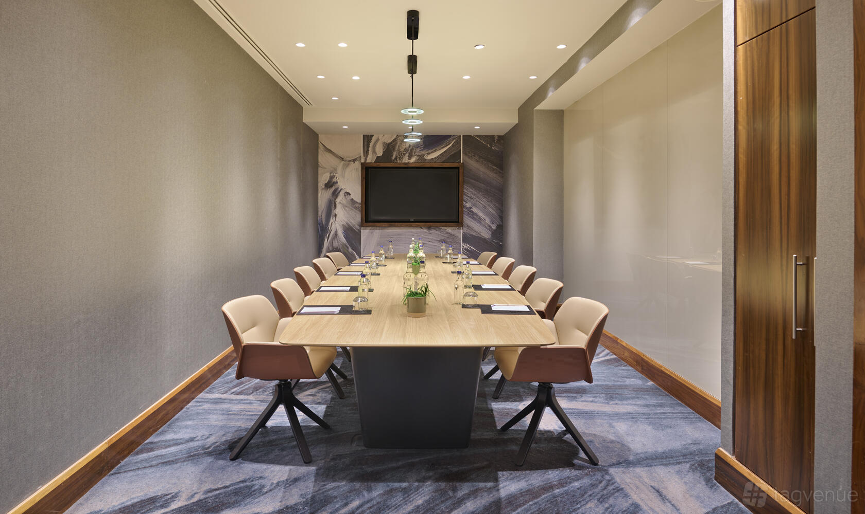 A boardroom with a long wooden conference table, plush swivel chairs, and wall-mounted screen at Hyatt Regency London Blackfriars.