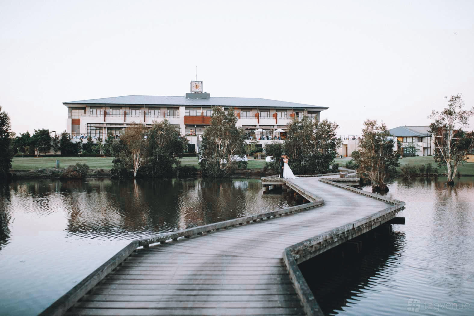 A hotel with a wooden footbridge over a lake leading to landscaped lawns at Mercure Kooindah Waters.