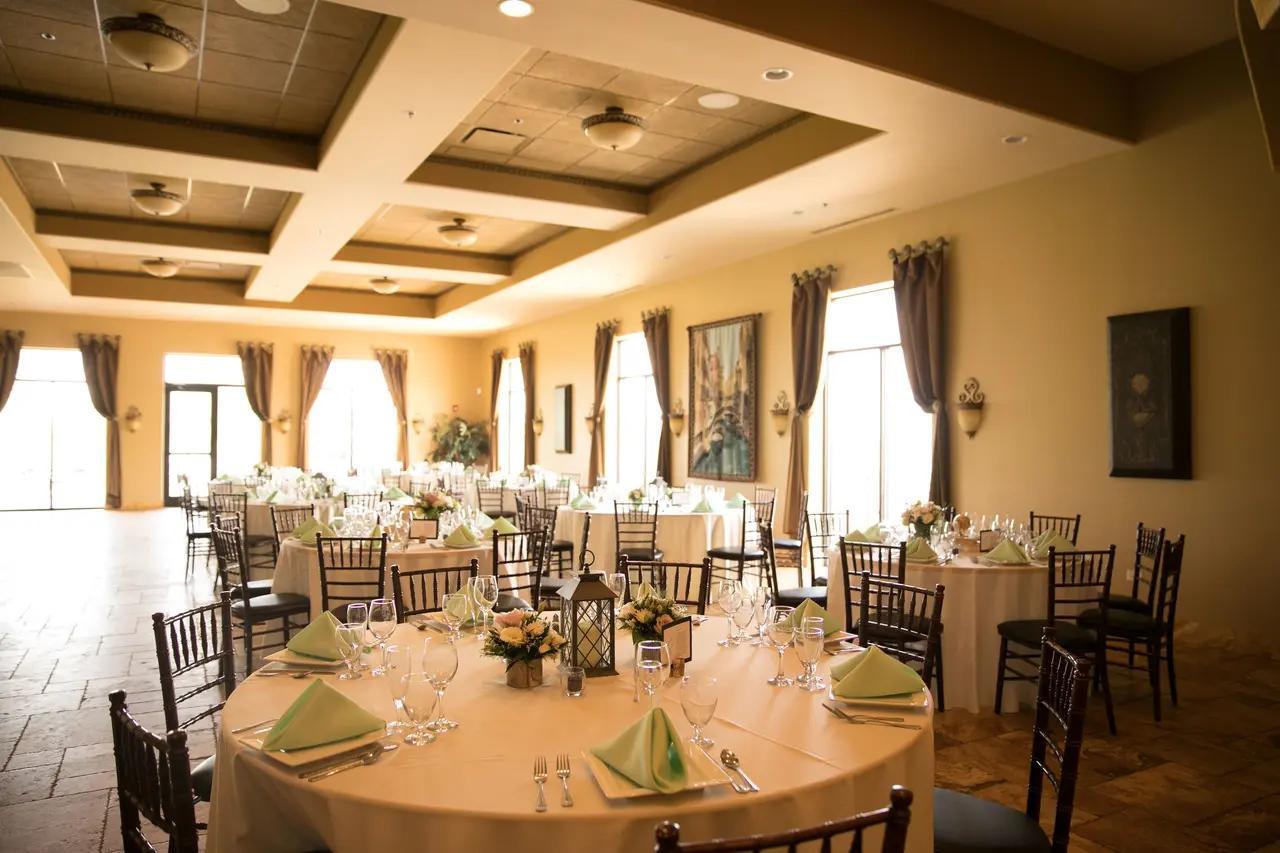An event venue with round tables set with white linens, floral centerpieces, and large windows at Acquaviva Winery.