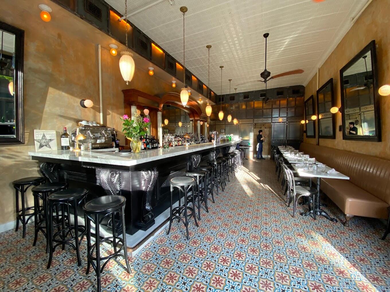A restaurant with a long marble-topped bar, patterned tile floor, hanging globe lights, and banquette seating at Ottava.