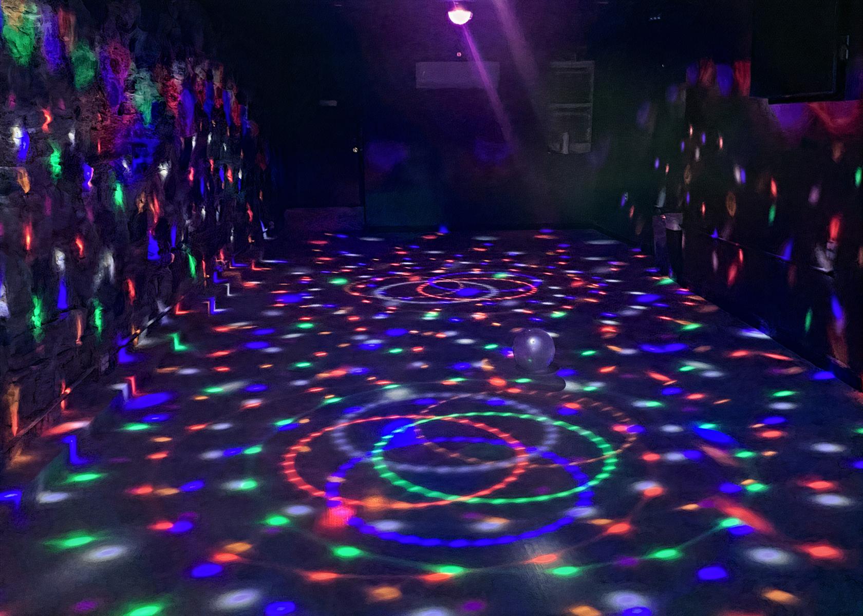 An event venue with colorful disco lights projected onto stone walls and a concrete floor at H I D D E N.