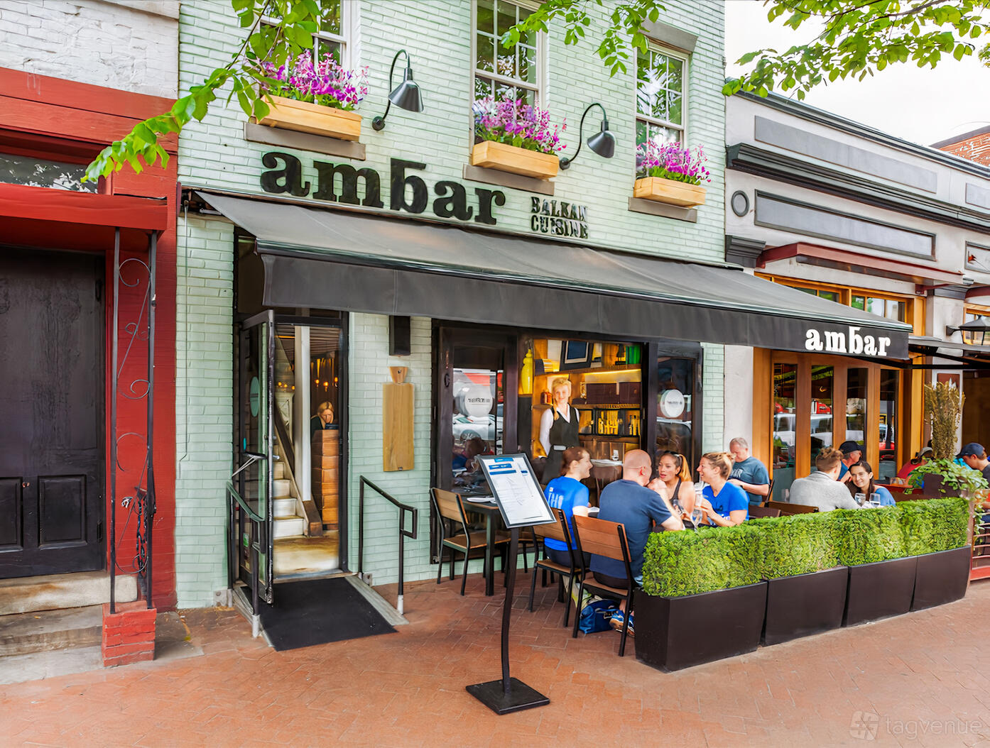 A restaurant with outdoor sidewalk seating, black awning, and flower boxes above the entrance at Ambar Capitol Hill.
