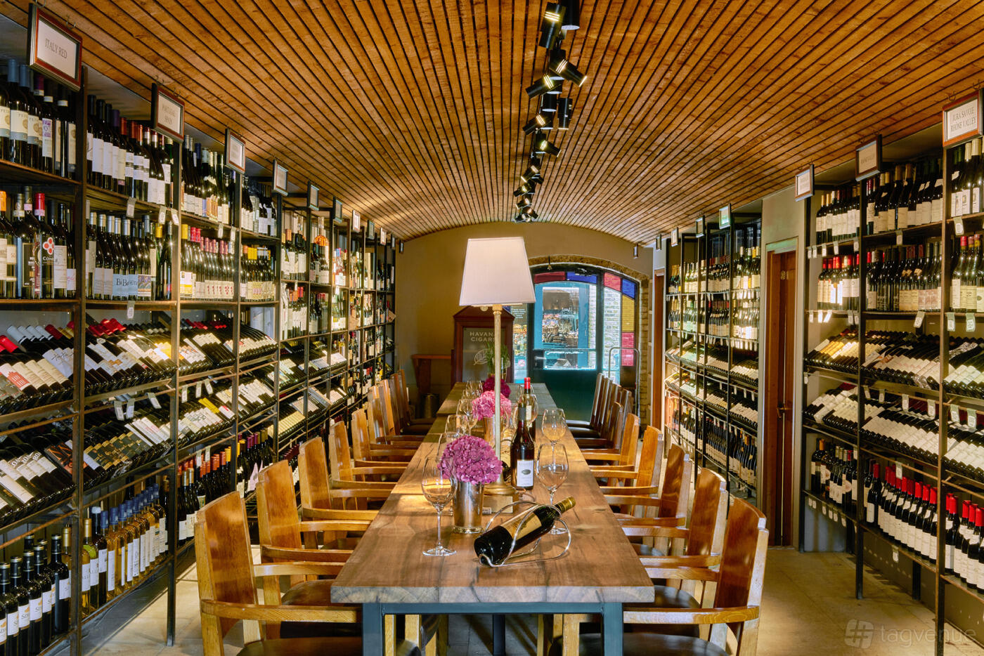 A wine cellar dining room with wooden chairs, a long table, and shelves lined with wine bottles at Le Pont de la Tour.