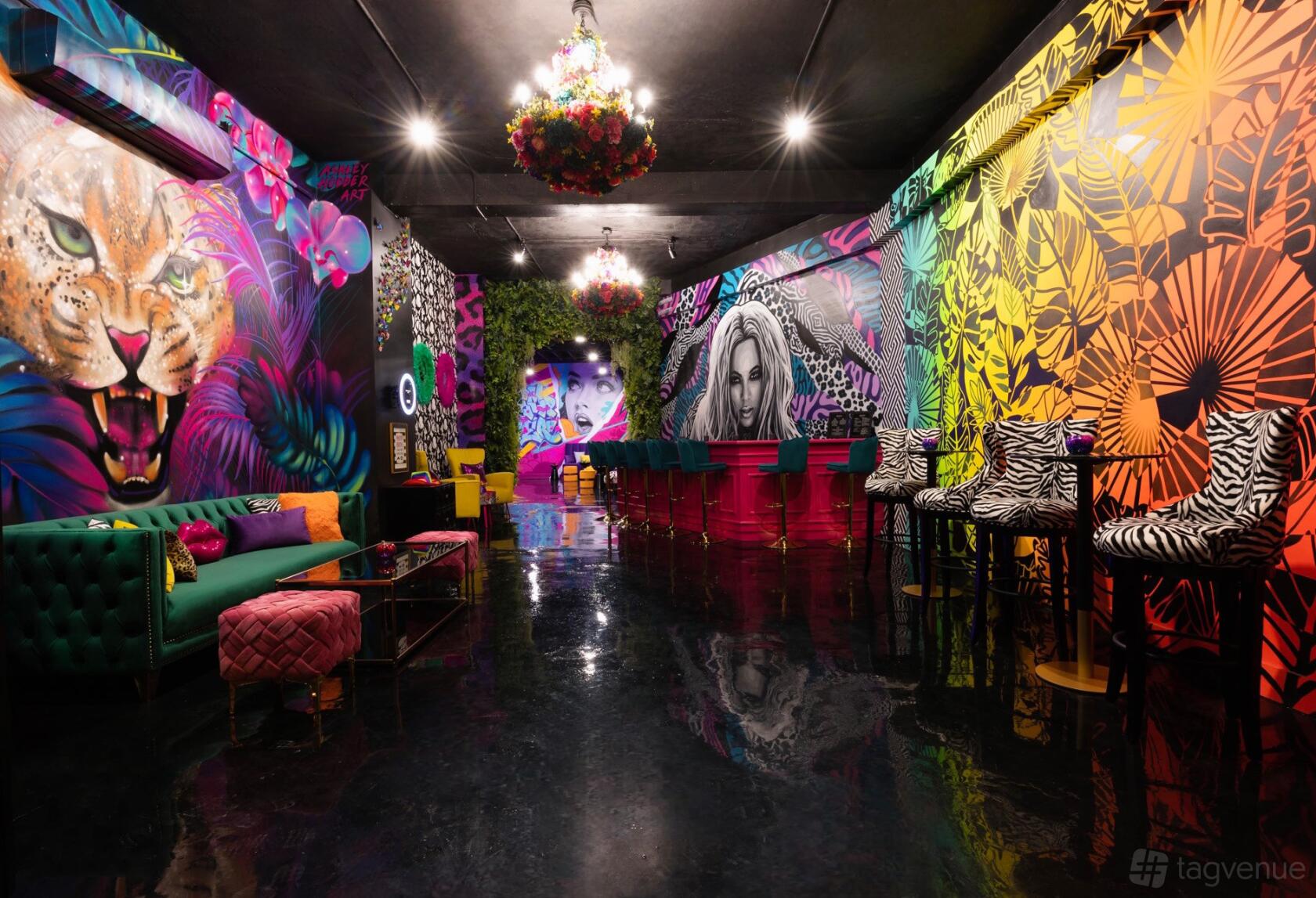 An event venue with colorful graffiti murals, velvet seating, chandeliers, and reflective floors at Social Cues - The Garden.