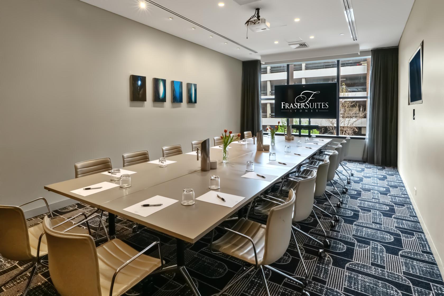 A boardroom with a long conference table, leather chairs, and floor-to-ceiling window at Fraser Suites Sydney.