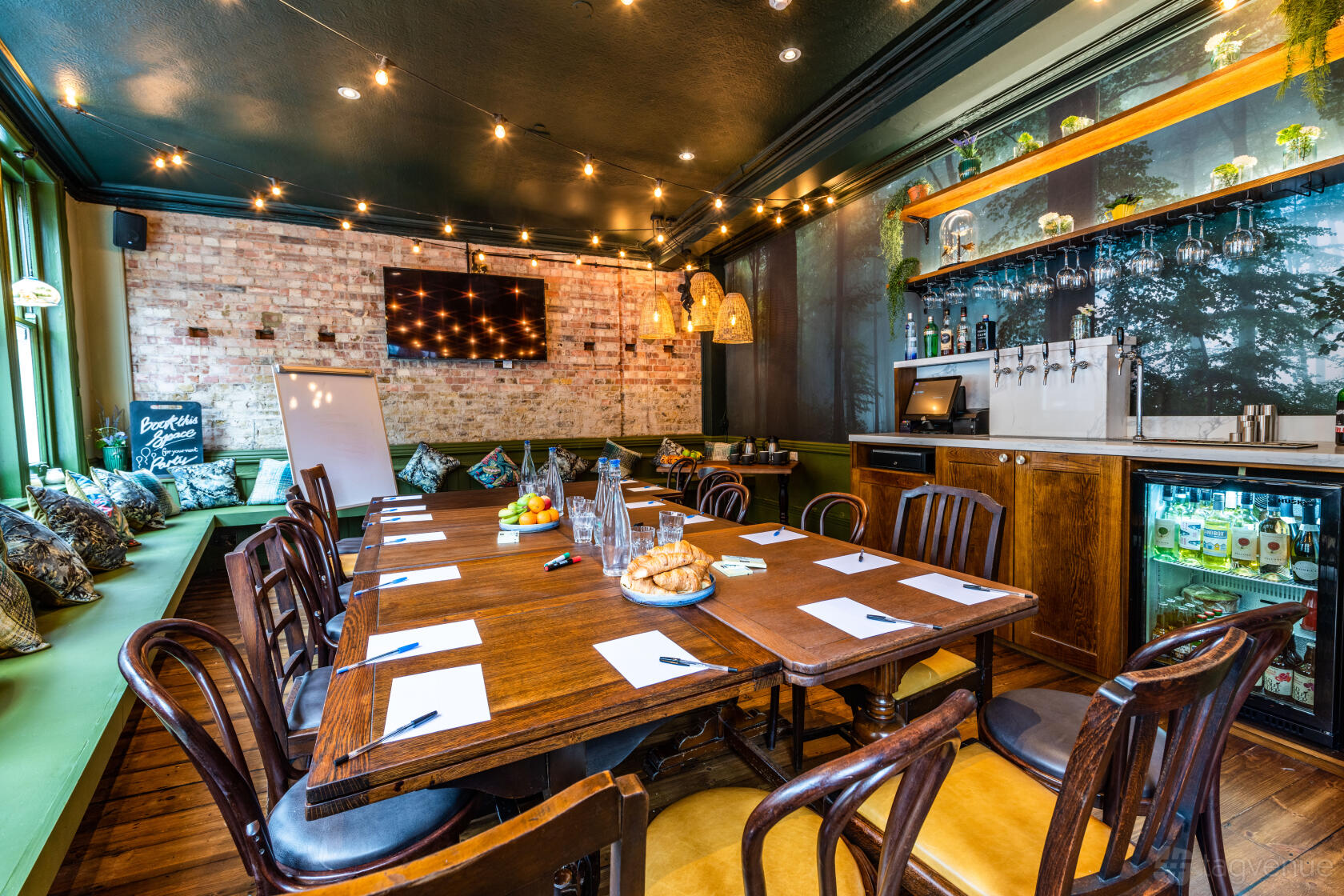 A function room in a pub with exposed brick walls, string lights, and a long wooden table at The Green Man.