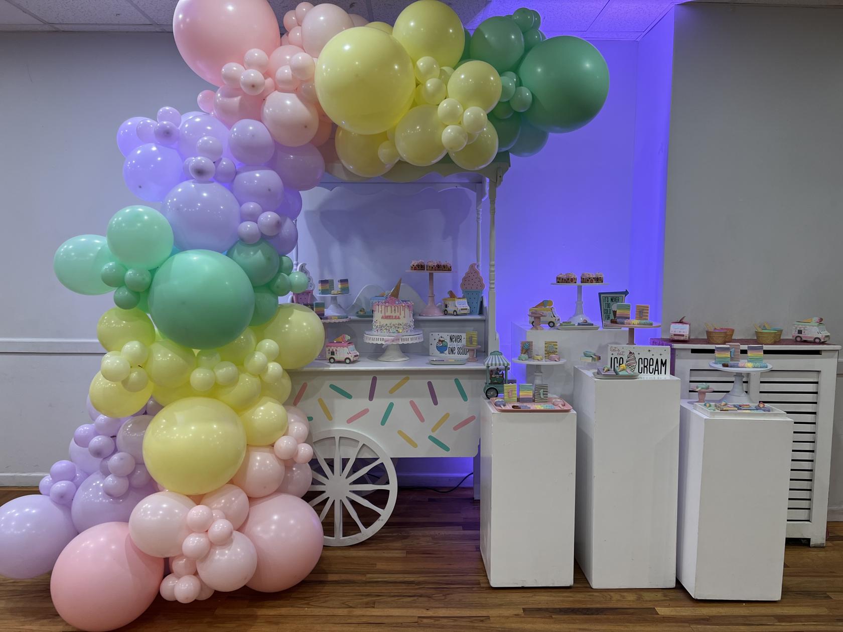 An event venue with a decorated dessert cart and pastel balloon arch at Party Solvers.