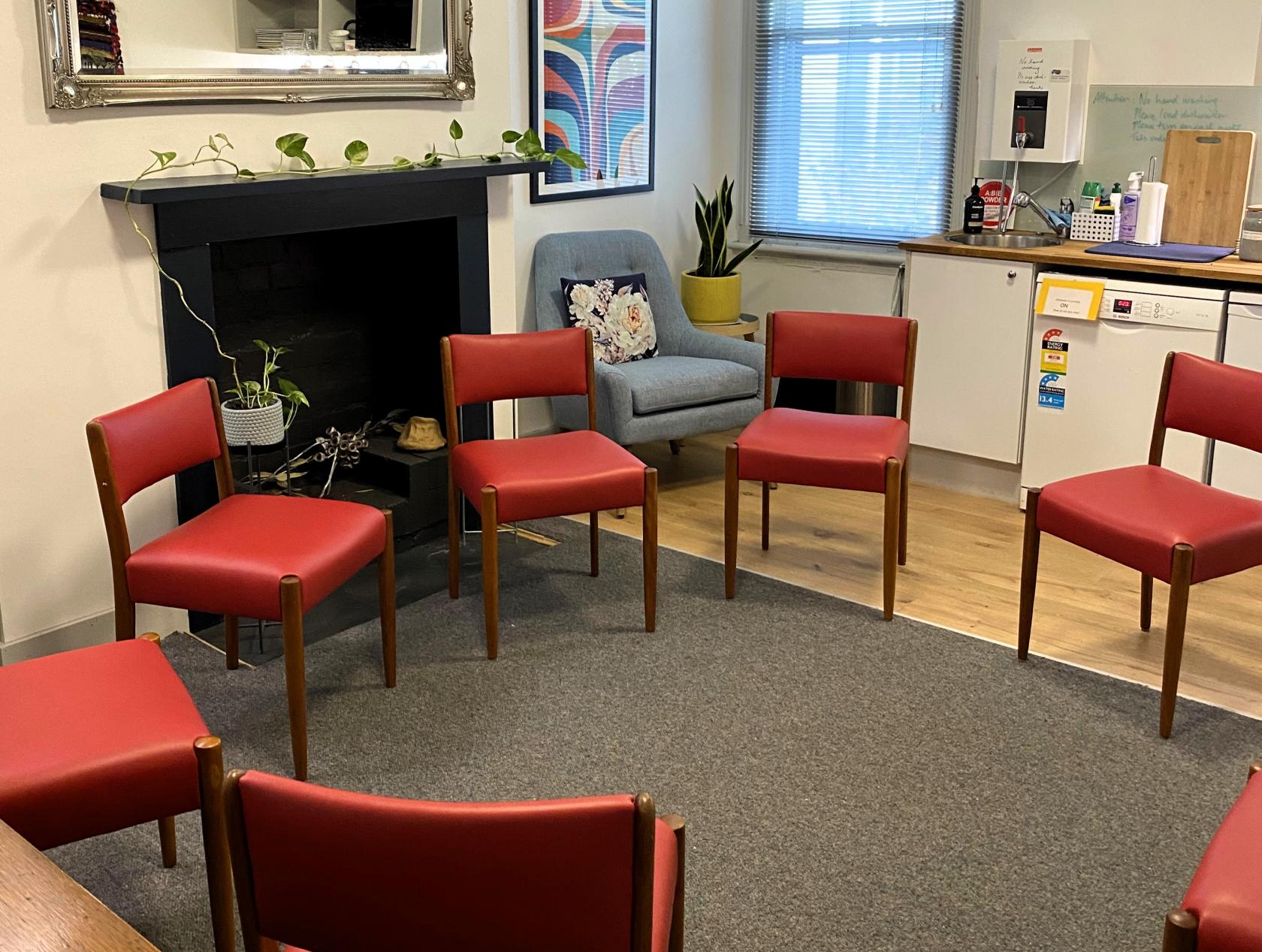 A therapy room with red chairs arranged in a circle, a small fireplace, and an armchair at Lygon Therapy.