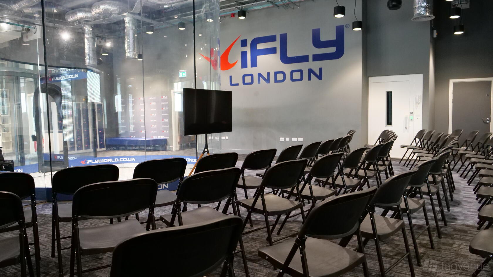 A meeting room with rows of black chairs facing a screen and large glass wall at iFLY Indoor Skydiving at The O2.