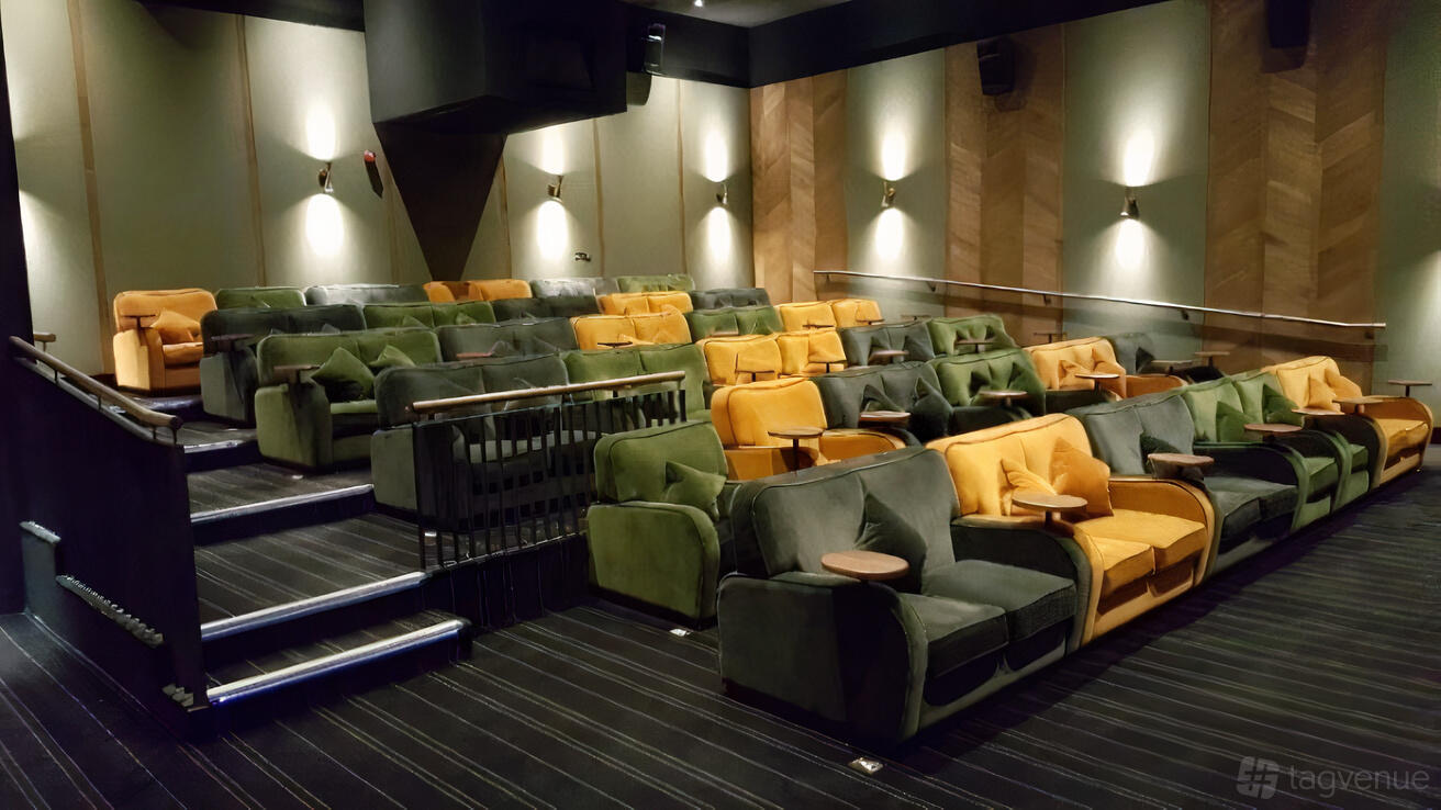 An auditorium with plush green and yellow velvet armchairs and side tables at Everyman Chelmsford