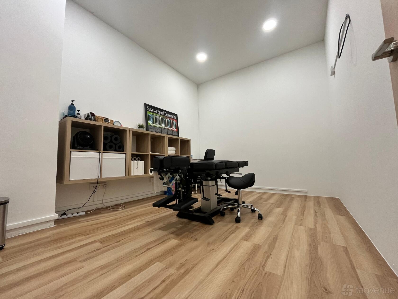 A therapy room with a black treatment table, light wood flooring, and floating shelves at The Training Room by CalGenie.
