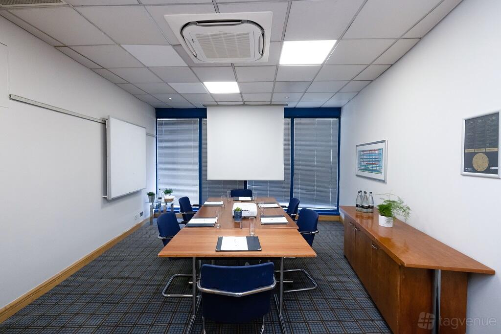 A hotel meeting room with a rectangular table, blue chairs, and a projection screen at Best Western Ariel London Heathrow.