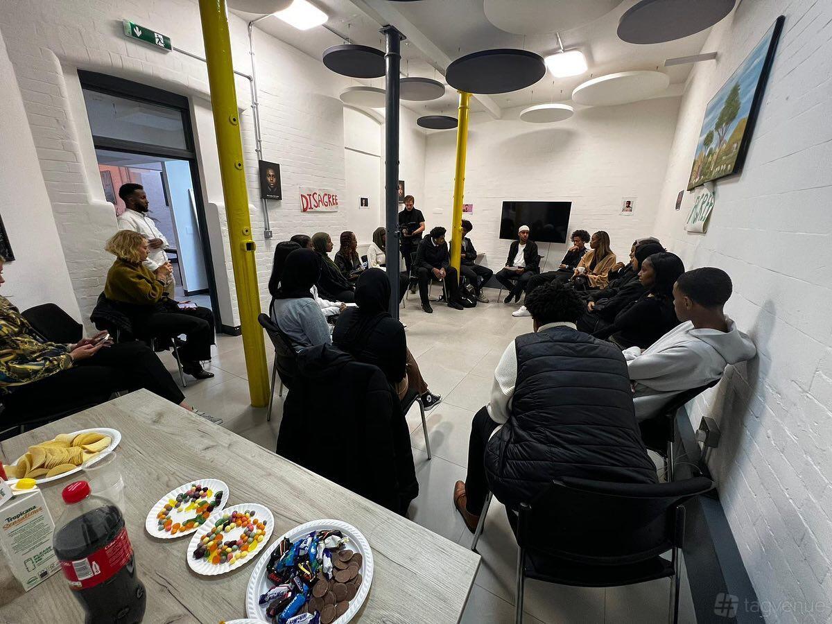A meeting room with white brick walls, round acoustic panels on the ceiling, and people seated in a circle at Culture House.