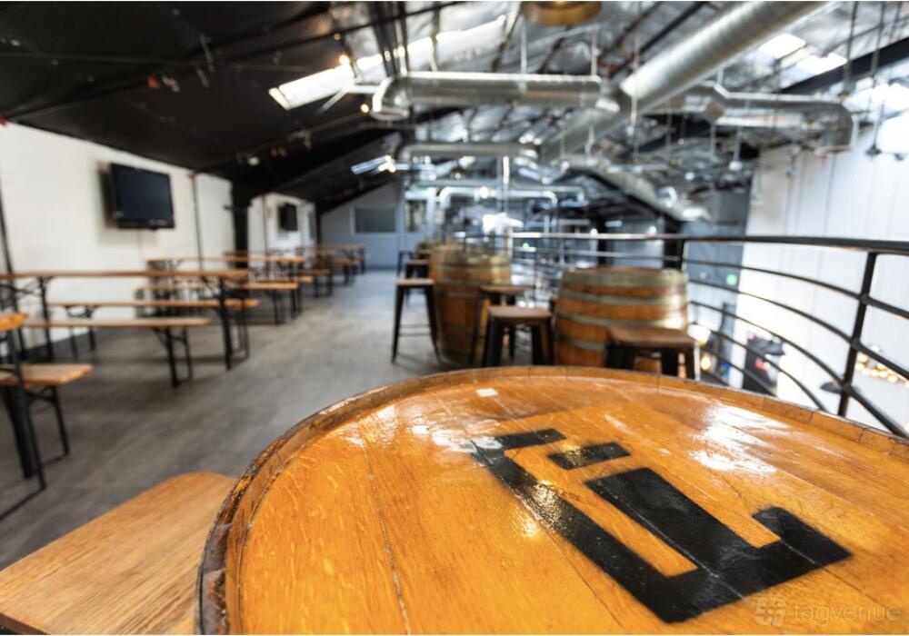 An event space with wooden barrel tables, bench seating, and exposed ductwork at Lawless Brewing Co.