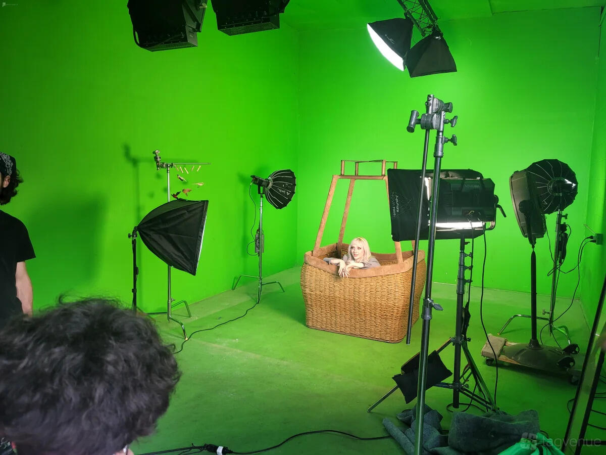 A photo studio with a green screen backdrop, softbox lights, and a wicker basket prop at Cosmic Cube Creative Studio.