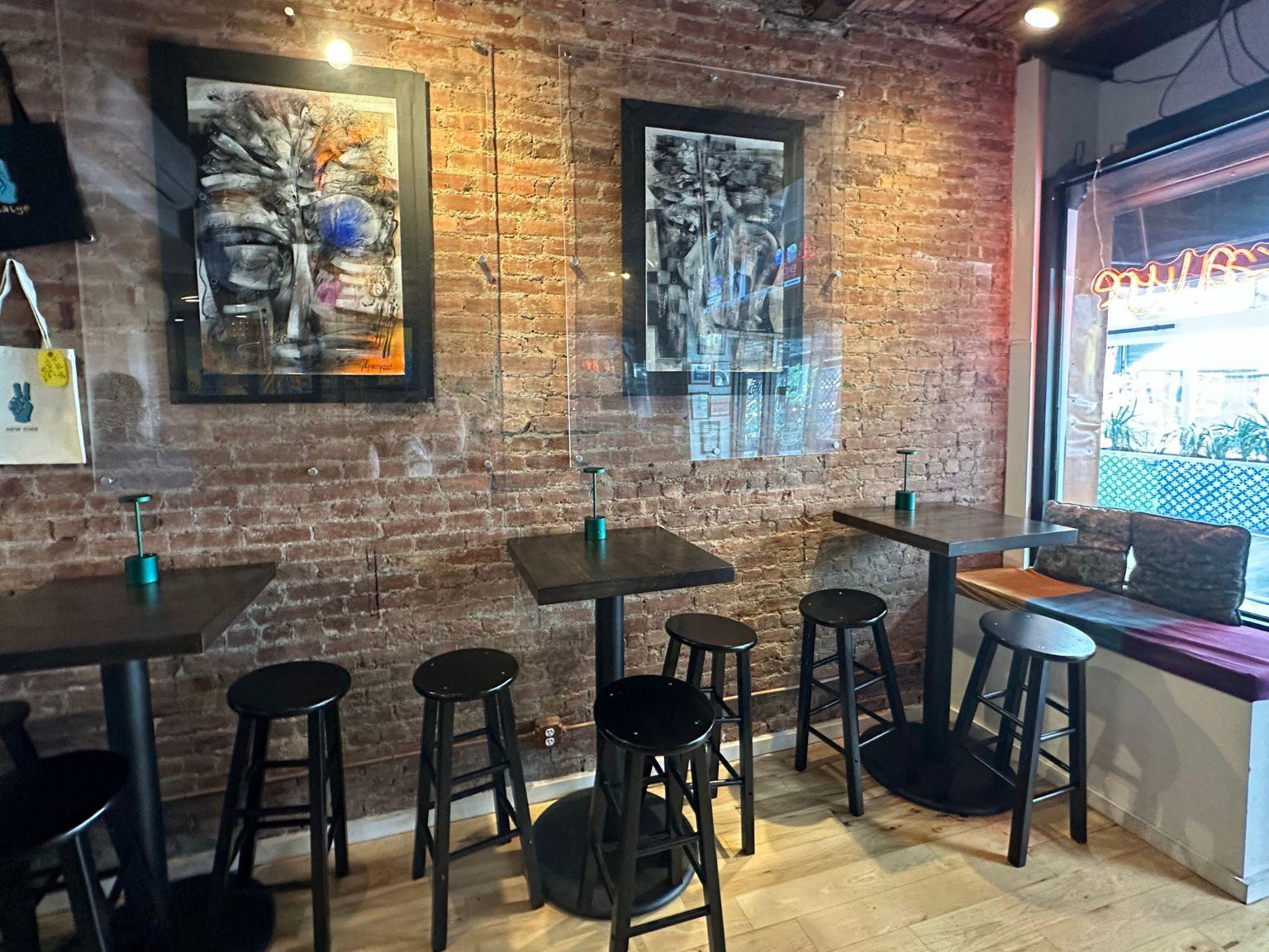 A restaurant with exposed brick walls, high-top tables, black stools, and framed artwork at Kalye.